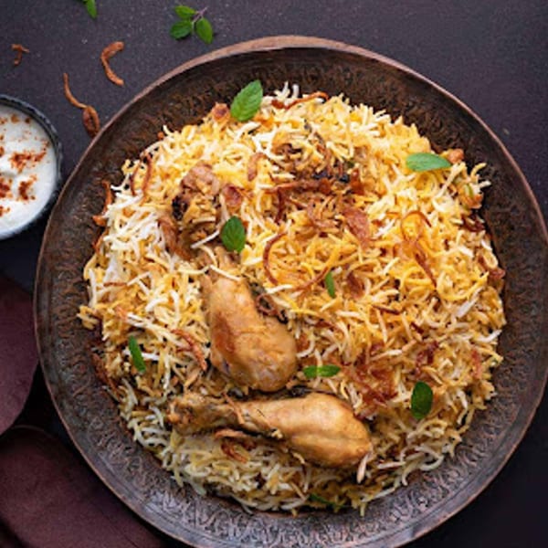 Chicken biryani with two drumsticks, rice, fried onions, and mint, served with raita.