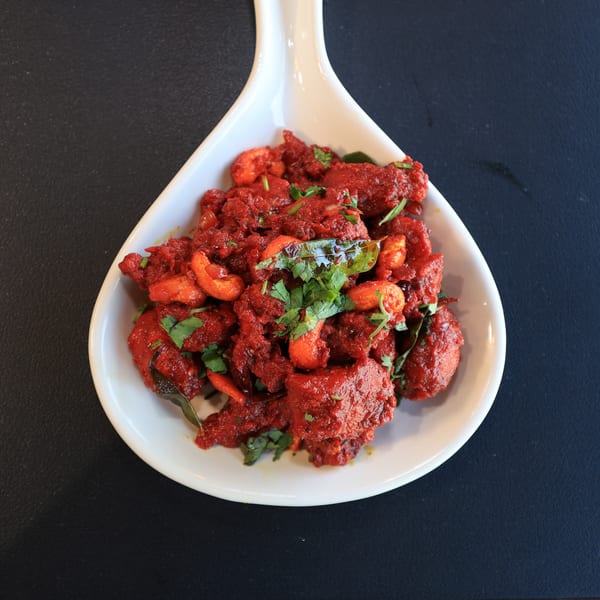Bright red Indian chicken dish with cashews and fresh herbs in a white serving bowl.